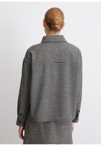 Black and white checkered jacket featuring a collared neck, long sleeves, and buttoned cuffs. Soft, textured fabric with a relaxed fit.