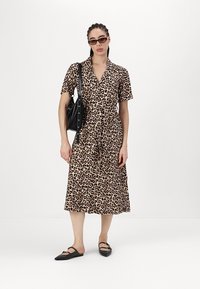 Liūto rašto midi suknelė su trumpomis rankovėmis, susiaurinta talija ir apykakle. Suderinta su juodais aksesuarais ir plokščiais bateliais. Lygus audinio paviršius.