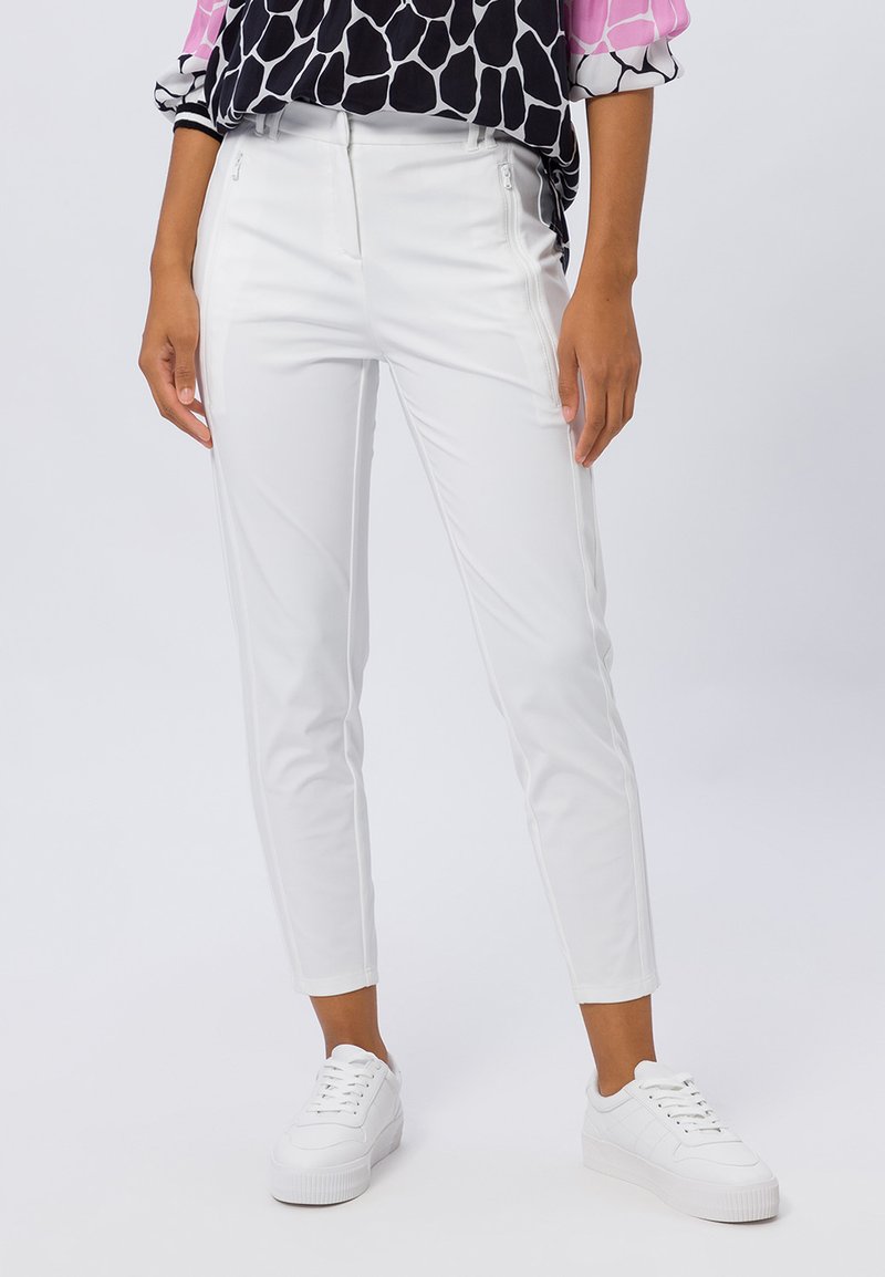 Witte, aansluitende broeken met een zachte textuur, voorzien van ritszakken en een cropped lengte, gecombineerd met witte sneakers.