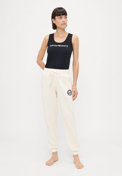 Čierny bezrukávový top s logom "Emporio Armani", skombinovaný s bielymi teplákmi na šnúrku s emblémom na ľavej nohe.