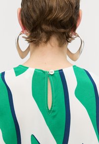 Πράσινη και λευκή τοποθετημένη μπλούζα με μπλε διακοσμητικές ρίγες, που διαθέτει κλείσιμο με κουμπί στο πίσω μέρος και λεπτομέρεια κλειδώματος στο λαιμό.