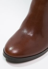 Bottine en cuir marron avec bout arrondi et semelle en caoutchouc noir sur fond blanc.