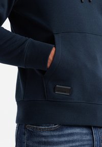Felpa blu navy realizzata in tessuto morbido, con tasca a marsupio, polsini a costine e un'etichetta nera vicino all'orlo.