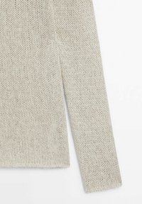 Manche longue de pull beige tricoté avec motif texturé sur fond blanc.