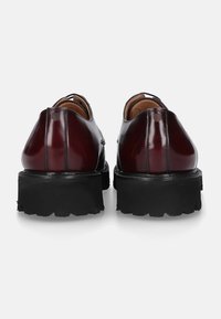 Burgunderfarbene Lederschuhe mit gl glossy Oberfläche, ausgestattet mit einer dicken schwarzen Gummisohle und schlichter Naht entlang der Nähte.