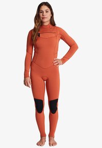 Brændt orange wetsuit lavet af stræk neopren, med høj krave, frontlynlås og sorte knæpuder. Tæt pasform.