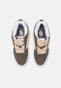 Brown suede sneakers with cream accents, beige laces, padded white collar, and white rubber soles. Vans logo on the tongue.
