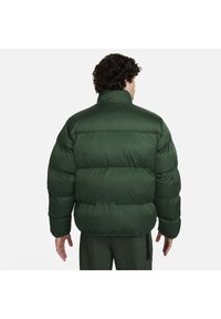 Zielona kurtka puchowa z wysokim kołnierzem, z pikowanym wzorem, pluszową teksturą i wyściółką. Brak widocznych logo lub akcentów.