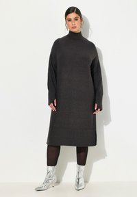 Robe tricotée longue et gris foncé avec un col haut, des accents en côtes au niveau de l'ourlet et des poignets, associée à des bottines argentées.