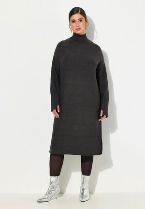 Robe tricotée longue et gris foncé avec un col haut, des accents en côtes au niveau de l'ourlet et des poignets, associée à des bottines argentées.