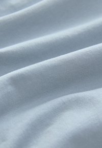 Lyseblødt blåt stof med fin strikket struktur og blide folder, der skaber subtile skygger og højdepunkter.