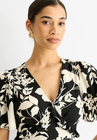 Schwarz-blumiges Kleid mit weißen botanischen Mustern, mit Puffärmel, tiefem V-Ausschnitt und geknotetem Taillendetail.