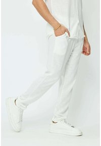 Pantalon en lin blanc avec une finition texturée, doté de poches latérales et d'une coupe fuselée, associé à des baskets blanches.