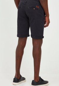 Dark navy shorts made from cotton, featuring rolled cuffs, back pockets with buttons, and a leather accent label. Worn with black sneakers.