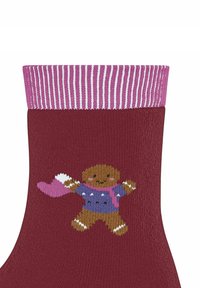 Bordowa skarpetka z różowym paskowanym mankietem przedstawia dzierganą postać piernikowego ludka w niebieskim swetrze i różowym szaliku, z wyciągniętymi ramionami.