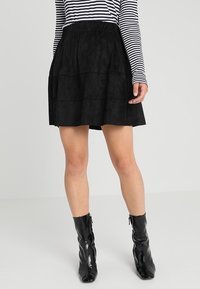 Musta kerroksellinen hame pehmeästä kankaasta, jossa on joustava vyötärö. Yhdistetty mustiin vetoketjullisiin nilkkasaappaisiin. Vaakasuoraan raidoitettu pitkähihainen paita.