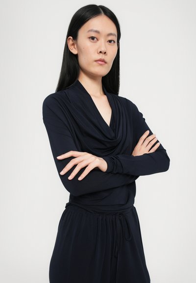 Long-sleeve navy top with draped neckline, soft texture, and fitted design, paired with matching loose-fitting pants and a drawstring waist.