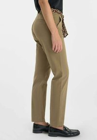 Pantalons kaki avec un design à jambe droite, dotés d'une ceinture en imprimé léopard noir et marron, associés à des mocassins noirs brillants. Texture lisse.