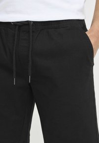 Svart shorts med snøring laget av lett stoff, med elastisk midje, sidelommer og en glatt tekstur.