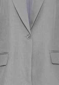 Blazer gris clair avec revers crantés, fermeture à un bouton et poches à rabat de chaque côté.