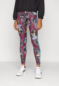 Leggings avec un imprimé de papillons colorés sur un fond marron foncé, ornés de rayures latérales turquoise contrastantes et d'un tissu extensible lisse.