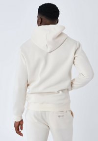 Felpa beige chiaro realizzata in tessuto morbido, con un ampio cappuccio, polsini a costine e una vestibilità rilassata, abbinata a pantaloni coordianti beige chiaro.