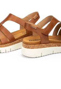 Sandalias de piel marrón con suela de corcho en cuña y base de goma blanca, con tiras ajustables y plantilla texturizada.