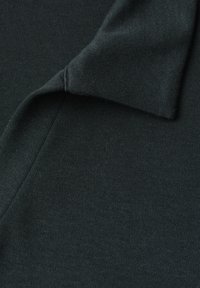 Tissu en maille gris foncé avec un détail de col plié montrant des coutures fines et la texture en gros plan.