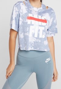 Camiseta corta de tie-dye azul claro con detalle de hombros recortados y texto audaz "MISFIT", combinada con leggins azul claro que presentan el logo "NIKE AIR".