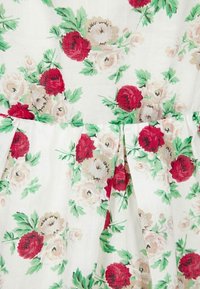 Kukallinen kangas, jossa on suuria punaisia ja kermaisia ruusuja sekä vihreitä lehtiä. Vaalea tausta, pehmeä rakenne, pussitetut muotoilut vyötäröllä.