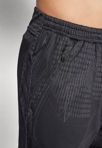 Zwarte sportbroek met een gestructureerd geometrisch patroon, elastische tailleband en een klein ritsvak aan de zijkant. Gladde stof, nauwsluitend ontwerp.