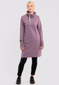 Lila, langärmliges Sweatshirtkleid mit einem Schalkragen, ausgestattet mit einer weißen Kordel und einem schwarzen Akzent am Ärmel. Schwarze Leggings und Schuhe.