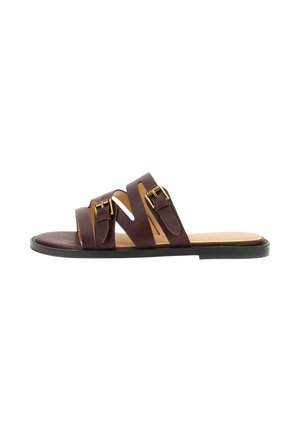 Brązowy skórzany płaski sandał z trzema regulowanymi paskami z pozłacanymi klamrami i czarną podeszwą, pokazany z profilu na białym tle.
