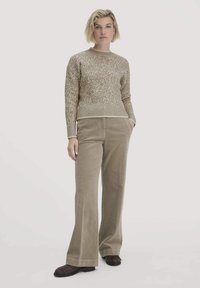 Beige gebreide trui met een textuurpatroon, gecombineerd met een wijde corduroy broek in een complementaire bruine tint. Het geheel is compleet met donkerkleurige schoenen.