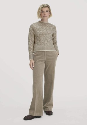 Beige Strickpullover mit einem strukturierten Muster, kombiniert mit weiten Cordhosen in einem passenden Braunton. Das Ensemble beinhaltet dunkle Schuhe.