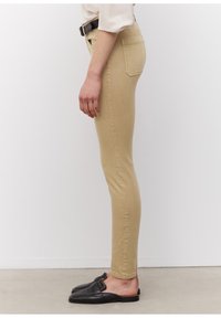 Béžové skinny džíny mají hladkou texturu, pět kapes a střední pas, doplněné černými nazouvacími botami.