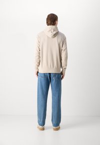 Krämfärgad hoodie med avslappnad passform och dragsko i huvan, kombinerad med ljusblå, löst sittande jeans och beige skor.