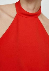 Rode halter-top met een gladde, textuurstof. Heeft een hoog kraagontwerp en strakke lijnen die de schouders accentueren.