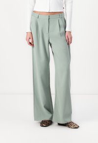 Pantalons larges vert clair avec des plis et une texture lisse. Associés à des ballerines imprimées léopard. Le tissu tombe délicatement.