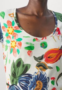 Camiseta con estampado floral en tejido ligero. Presenta un escote amplio, colores vibrantes incluyendo rojo, azul y verde, con un pequeño detalle bordado.