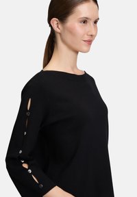 Czarny sweter dzianinowy z okrągłym dekoltem, rękawami do trzech kwart, z guzikami na accentach oraz wycięciami na ramionach.