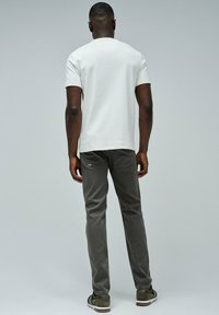 Camiseta blanca de manga corta, pantalones ajustados grises, zapatos verde oliva. Diseño simple, textura suave y detalles de costura sutiles visibles.