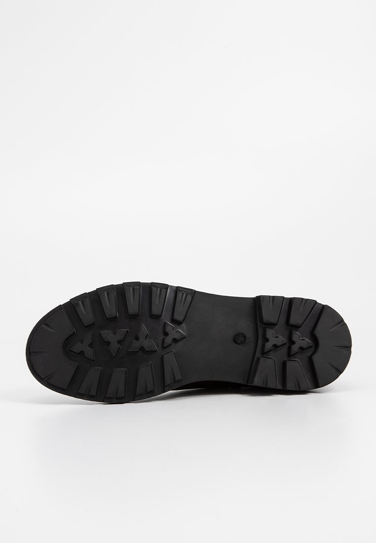 Schwarze Gummisohle mit einem robusten Profil und ausgeprägten Grip-Elementen, die verschiedene Traktionselemente und einen glatten zentralen Bereich aufweist.