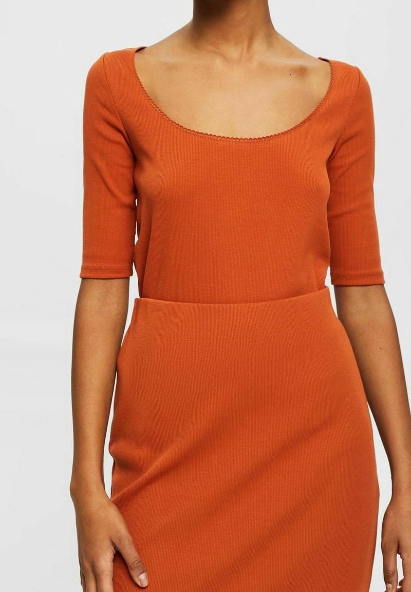 Robe orange côtelée avec un décolleté carré, des manches courtes et un corsage ajusté, présentant une texture lisse et un détail subtil à l'ourlet.