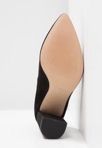 Chaussure femme en daim noir à bout pointu vue de la semelle avec un petit talon carré et une semelle extérieure beige texturée.