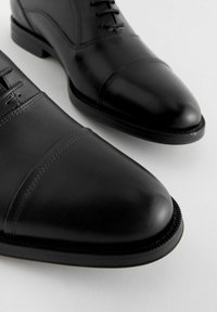 Black leather dress shoes with a smooth finish, rounded toe, straight laces, and decorative stitching across the upper.