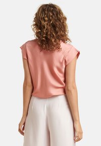 Korte mouwen, lichtroze blouse met een zachte textuur en een ontspannen pasvorm, gecombineerd met crèmekleurige wijde broekspijpen. Minimalistisch ontwerp, zonder zichtbare patronen.