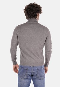 Maglioncino grigio aderente con colletto alto e maniche lunghe, realizzato in un materiale a maglia liscia, abbinato a jeans blu. Viene mostrata la vista da dietro.