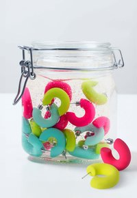Boucles d'oreilles en silicone colorées dans des nuances de rose, vert et bleu, présentées dans un pot transparent avec des bulles, dotées d'attaches en métal argenté.
