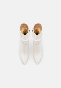 Bottes blanches à cheville avec un bout pointu et un design souple plissé. Dotées d'une fermeture éclair latérale et d'une texture en cuir lisse avec une doublure intérieure couleur beige.